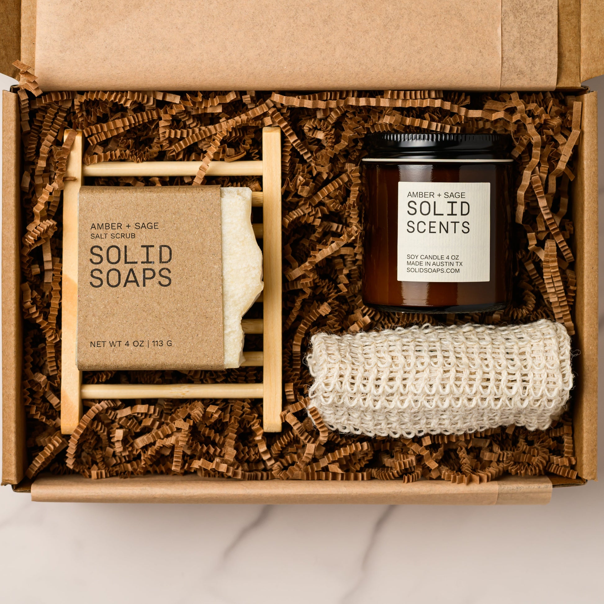 Open box containing solid soaps and a jar of solid scents candle on a marble surface