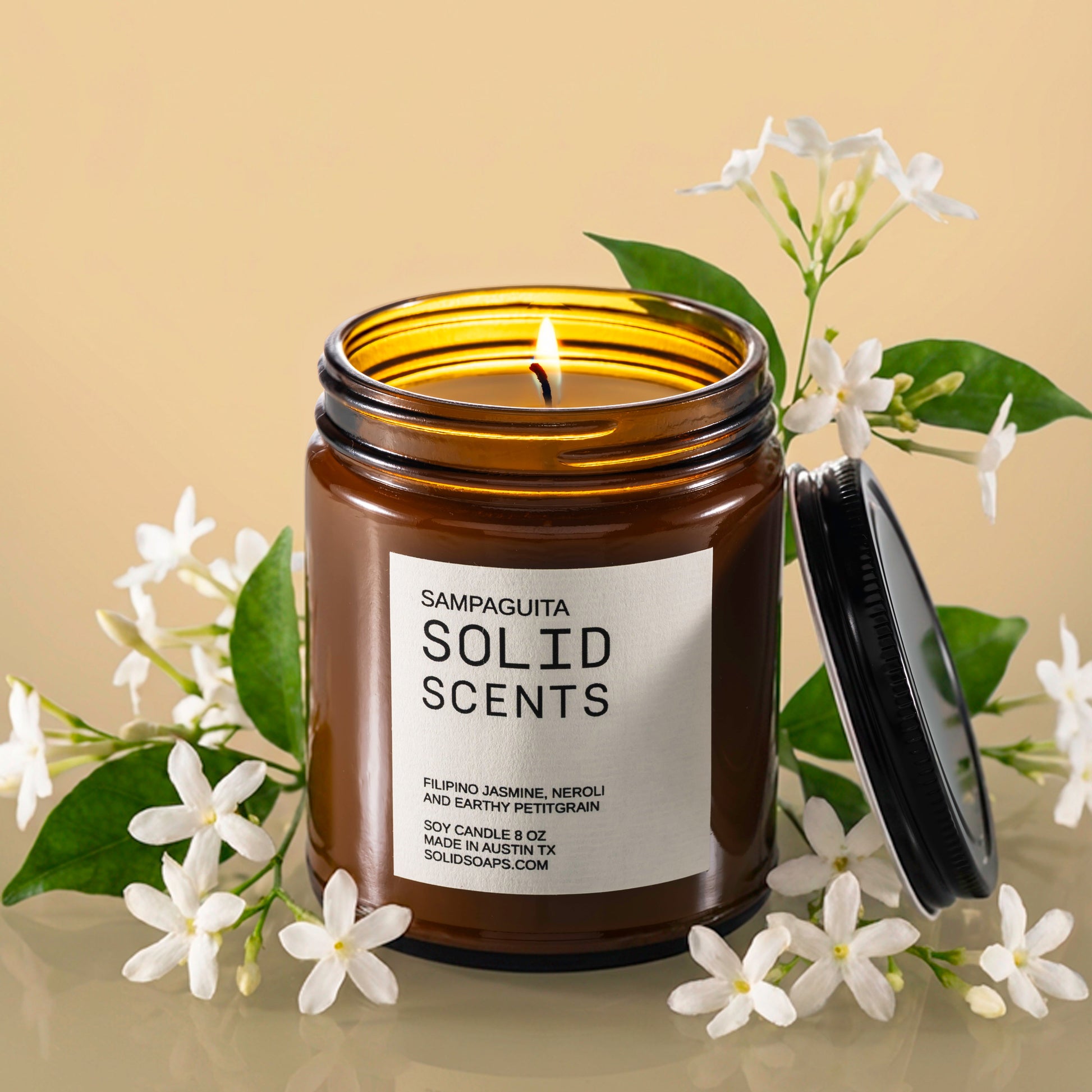 Solid Scents Sampaguita candle with a lid on a reflective surface with flowers around